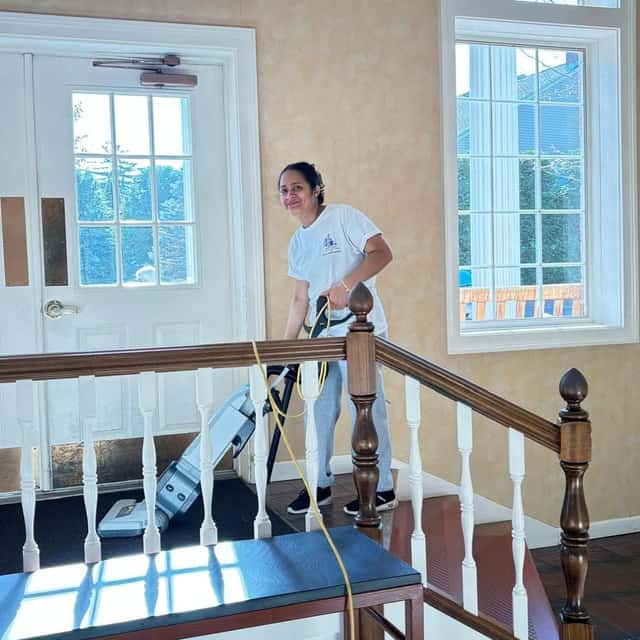 Vacuuming a stair landing beside tall windows — MARTS-R.P Cleaning Solutions LLC